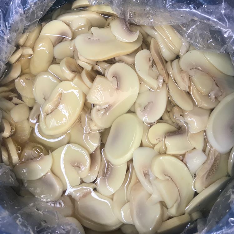 Sliced white champignon mushroom in salted water in drums Sliced white champignon mushroom in salted water in drums